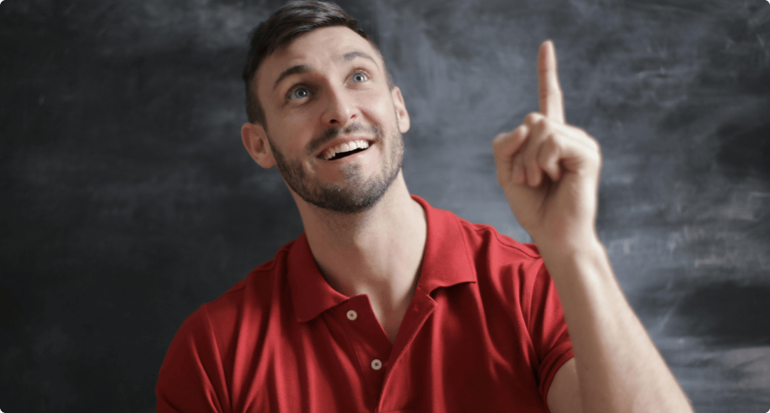 Smiling man in a red polo shirt pointing upward with a thoughtful expression against a chalkboard background.